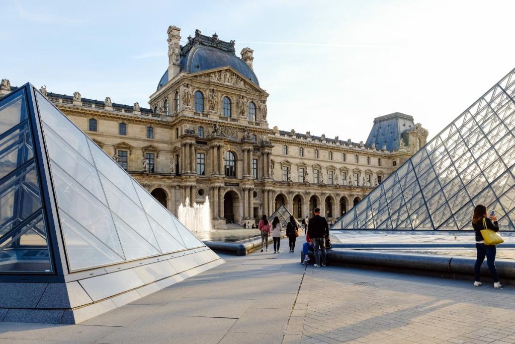 A view between the two glass pyramids outside of The Louvre in Paris looking at the majestic building.